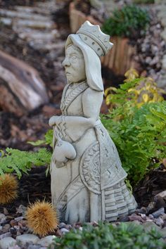 a statue sitting on top of a pile of rocks next to flowers and plants in a garden