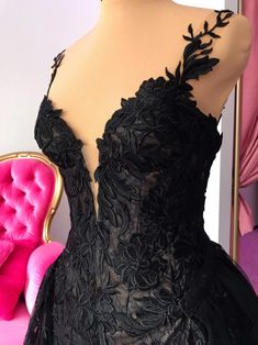 the back of a black evening gown on display in front of a pink velvet chair