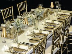 the table is set with gold and white plates, napkins, silverware, and vases