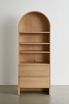 a wooden bookcase sitting on top of a cement floor next to a white wall