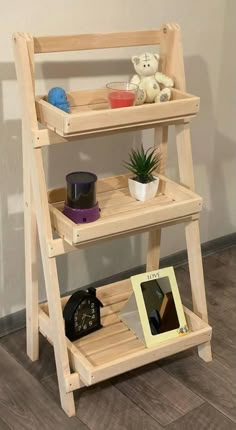 a three tiered wooden shelf with pictures and toys on the bottom shelf, next to a small potted plant