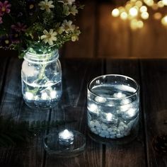 two mason jars filled with rocks and flowers on a wooden table next to a lit candle