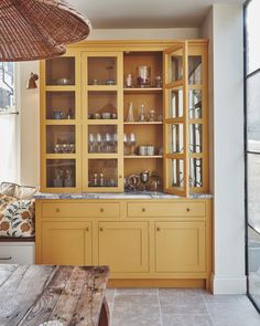 a wooden table sitting in front of a yellow book shelf filled with glasses and dishes