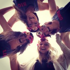 four girls are standing in a circle with their hands on their hipss and wearing flower leis