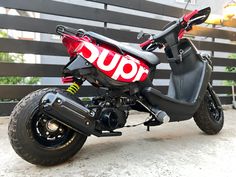 a red and black motor scooter parked in front of a fence