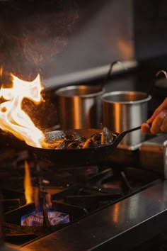 a person cooking food in a wok on top of a stove with flames coming out of it