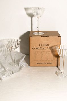 four wine glasses sitting on top of a table next to a cardboard box with the words cosmo cordial cooler written on it