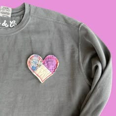 a gray sweatshirt with a patched heart on the front and back side, sitting against a pink background