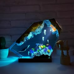 an illuminated glass sculpture with fish and corals in the water on a table next to a brick wall