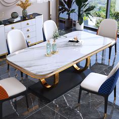 a dining room table with white chairs and gold trim around the edges, in front of a large window