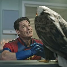 a man with an eagle on his arm next to a bird that is sitting on top of a table