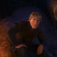 a young boy sitting on the ground next to a horse in a barnyard at night