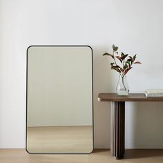 a mirror sitting on top of a wooden table next to a vase with flowers