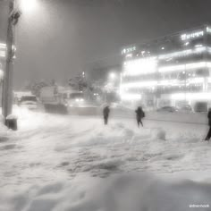 people are walking through the snow at night in front of a building with lights on