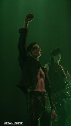 two shirtless men on stage with one holding his arm up in the air while another holds