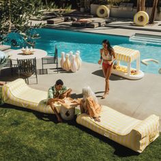 three people sitting on yellow and white striped chaise lounges next to a pool