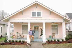 a woman standing on the front porch of a pink house with white pillars and columns