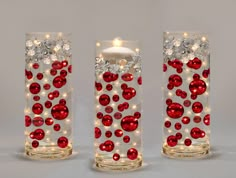 three glass vases with red and white ornaments on the sides, one holding a lit candle