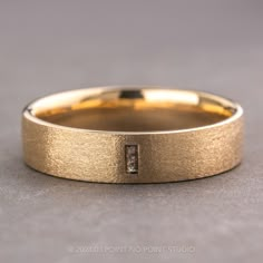 a yellow gold wedding band with a diamond in the center on a gray surface,