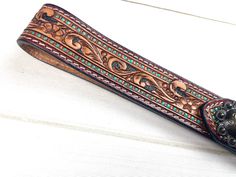 a brown leather belt with blue and green beads on the bottom, sitting on a white surface