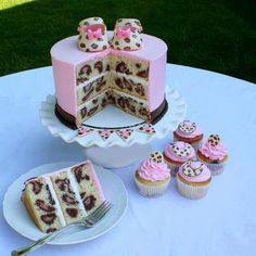 a pink cake and cupcakes on a table with grass in the back ground