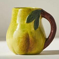 a green and brown ceramic mug with a leaf on the handle, sitting on a white surface