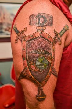 a man with a tattoo on his arm has a shield and two swords in front of him