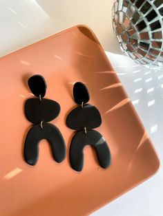 two black earrings are sitting on a pink plate