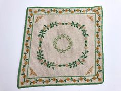 an embroidered placemat on a white surface with green and orange flowers in the center