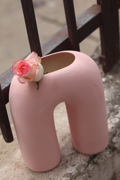 a pink vase with a flower sticking out of it's mouth sitting on a bench