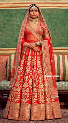 a woman in a red and gold bridal gown standing next to a couch with a green wall behind her