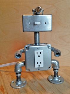 a robot made out of metal pipes on a wooden floor with a light switch plugged in