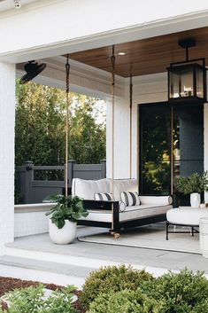 a porch swing with pillows and potted plants on the front porch, next to an outdoor living area