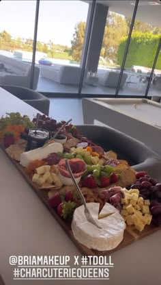 a platter filled with fruit and cheese on top of a table next to a window