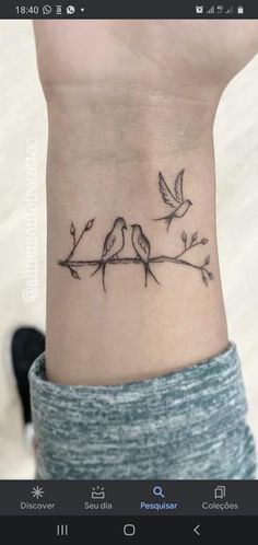 a wrist tattoo with two birds sitting on top of the branch and one bird flying above it