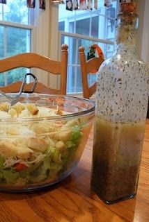 a salad in a glass bowl on a wooden table with a bottle of dressing next to it