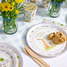 a table topped with plates and vases filled with yellow flowers on top of a blue checkered table cloth