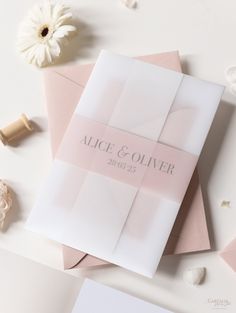 the wedding stationery is laid out on top of pink envelopes and white flowers