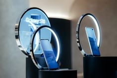 two cell phones on pedestals with circular mirrors in the background and lighting around them