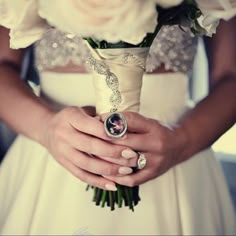 a woman in a wedding dress holding a bouquet of flowers and a ring on her finger