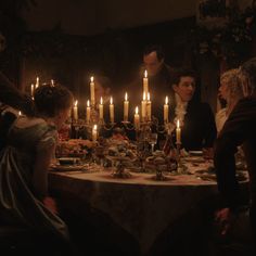 a group of people sitting around a dinner table with candles on top of the table