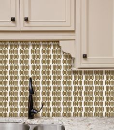 a kitchen sink under a faucet in front of a wallpapered backsplash