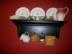 a shelf filled with dishes and cups on top of a red wall