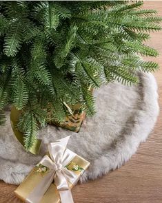 a christmas tree with presents wrapped in gold and white ribbons on it, sitting next to a fur rug