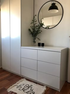 a white dresser sitting next to a round mirror on top of a wooden floor in a room