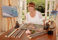 a woman sitting at a table with some art on it and paintings in the background