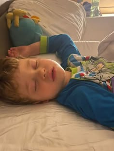 a young boy laying on top of a bed next to a stuffed animal toy in his hand