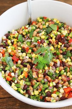 a white bowl filled with beans, corn and cilantro on top of a wooden table