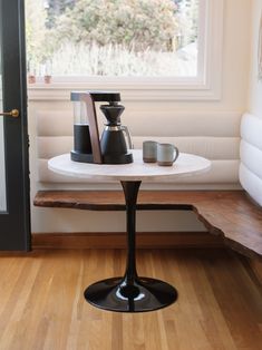 a table with two coffee pots on it in front of a window and wooden bench