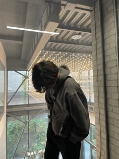 a young man standing in front of a window looking at something on the ground below